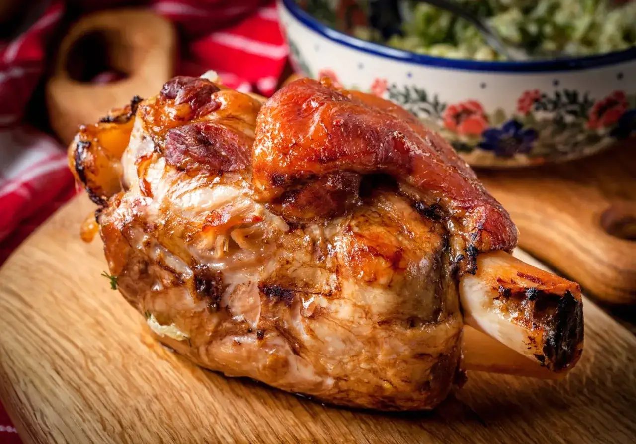 Stinco di maiale al forno, dorato e succulento, pronto per essere gustato. Accompagnato da un'insalata fresca in una ciotola decorata.