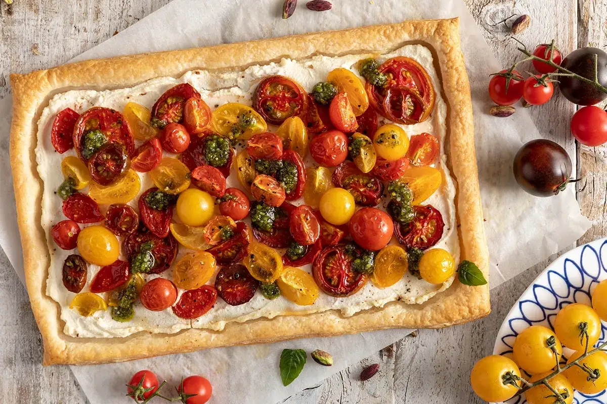Torta salata con ricotta al forno, pomodorini colorati e pesto. Un tripudio di sapori mediterranei su pasta sfoglia dorata.