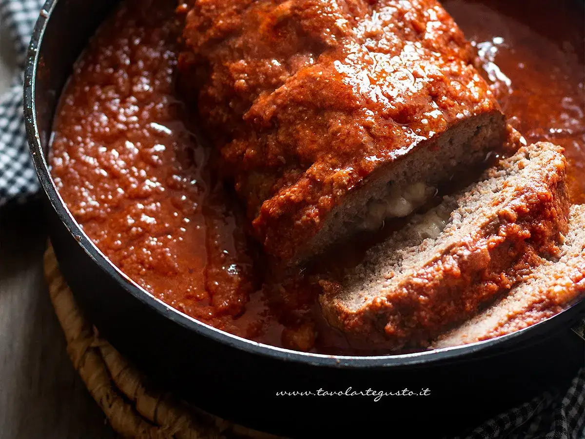 Polpettone in padella, succulento e ripieno di formaggio filante, immerso in un sugo rosso intenso.