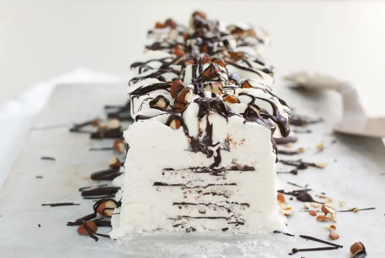Un delizioso semifreddo al cioccolato, con strati di gelato bianco e scaglie di cioccolato fondente, guarnito con mandorle tostate e una cascata di salsa al cioccolato.