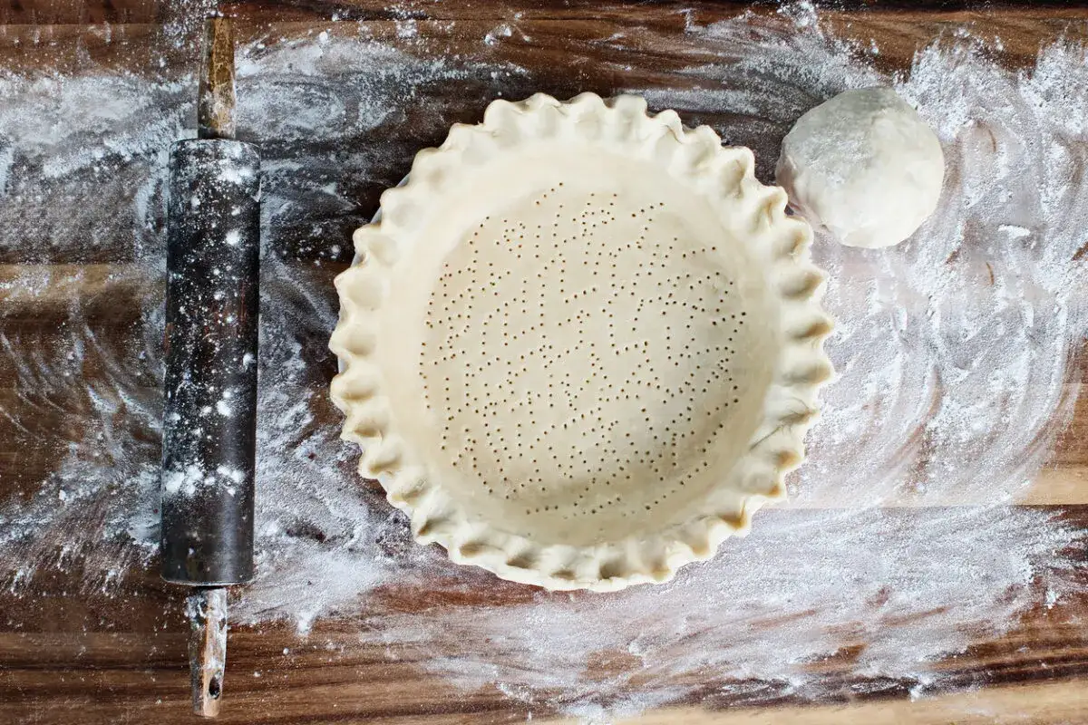 Pasta frolla senza glutine pronta per essere infornata. Un mattarello e un impasto a forma di palla completano la scena.