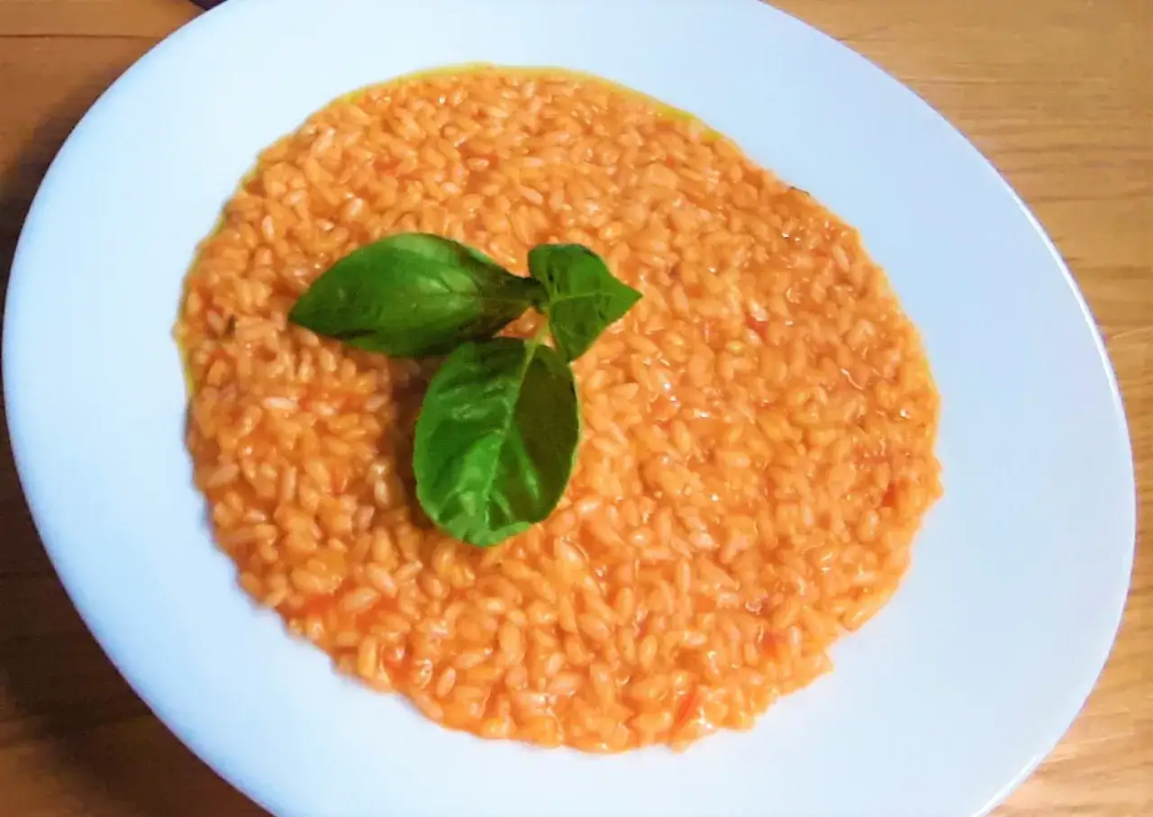 Un cremoso risotto al pomodoro, guarnito con foglie di basilico fresco, servito su un piatto bianco.