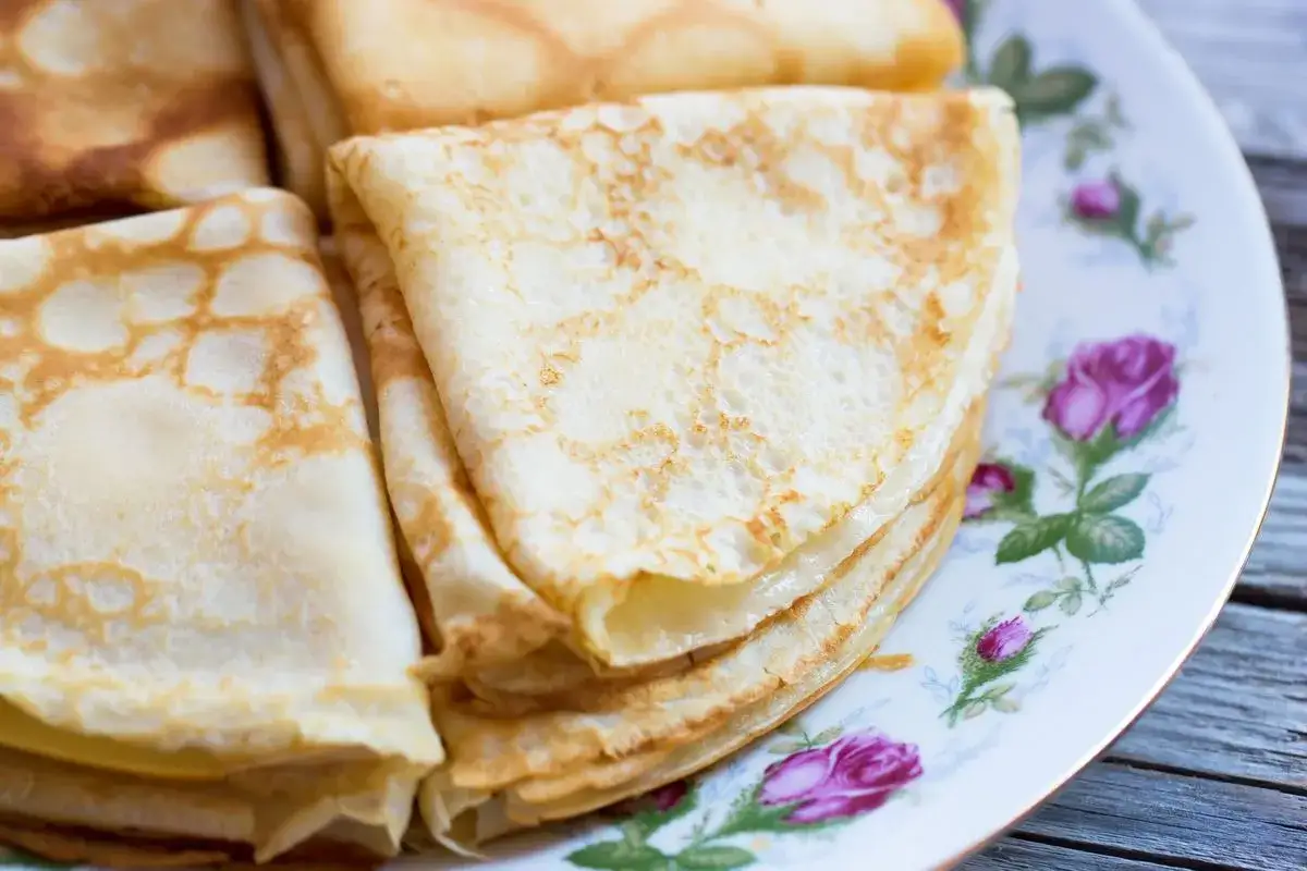 Piatto di crepes senza latte, piegate a triangolo, su un piatto decorato con rose.