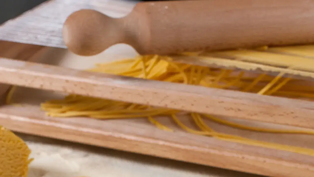 Pasta fatta in casa senza macchina, con mattarello in legno e fili dorati pronti per essere gustati.