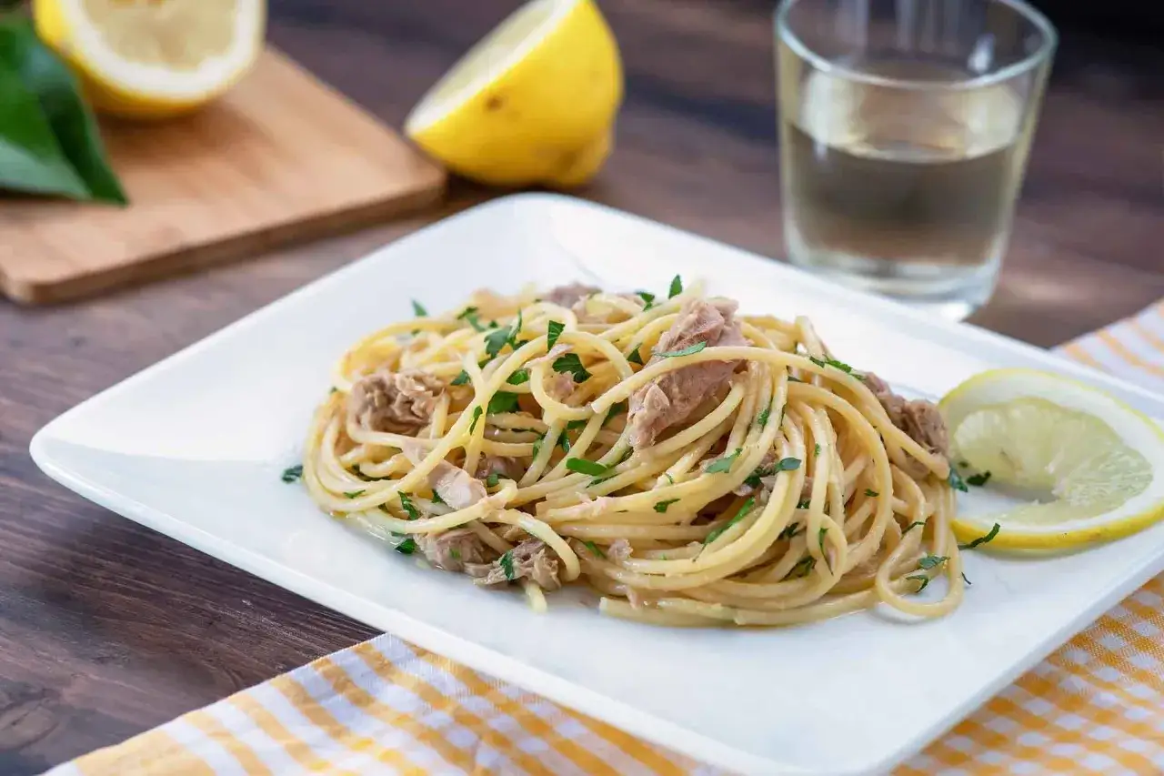 Un piatto invitante di pasta tonno e limone, guarnito con prezzemolo fresco e spicchi di limone.