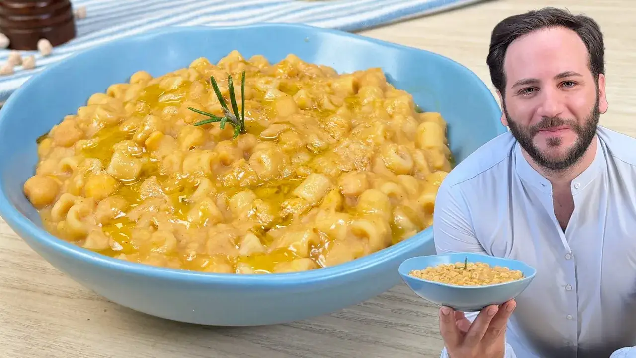 Un uomo sorridente mostra una ciotola di pasta e ceci fumante, guarnita con rosmarino e un filo d'olio.