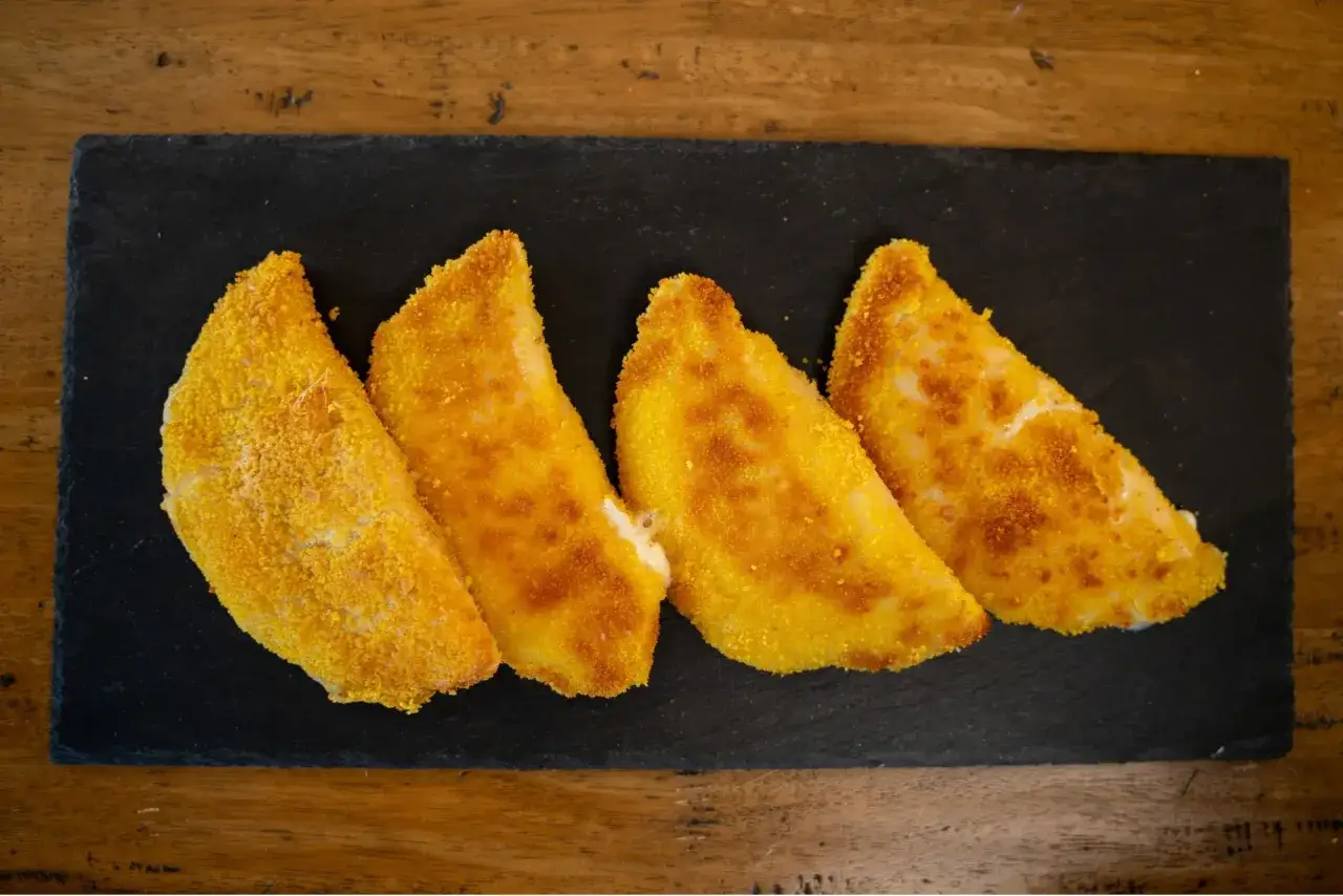 Quattro sofficini fatti in casa dorati e croccanti, serviti su una pietra nera.