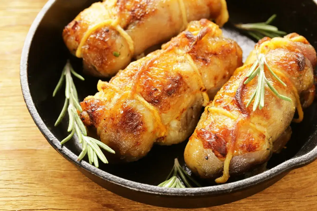 Involtini di pollo dorati e succulenti, legati con spago da cucina e guarniti con rametti di rosmarino, in una padella di ghisa.