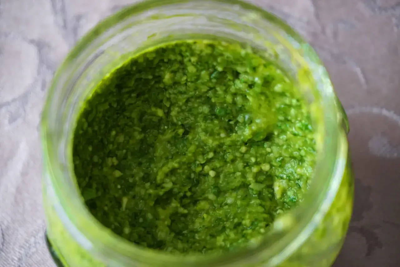 Vaso di vetro pieno di vibrante pesto di basilico fatto in casa, pronto per condire la pasta.