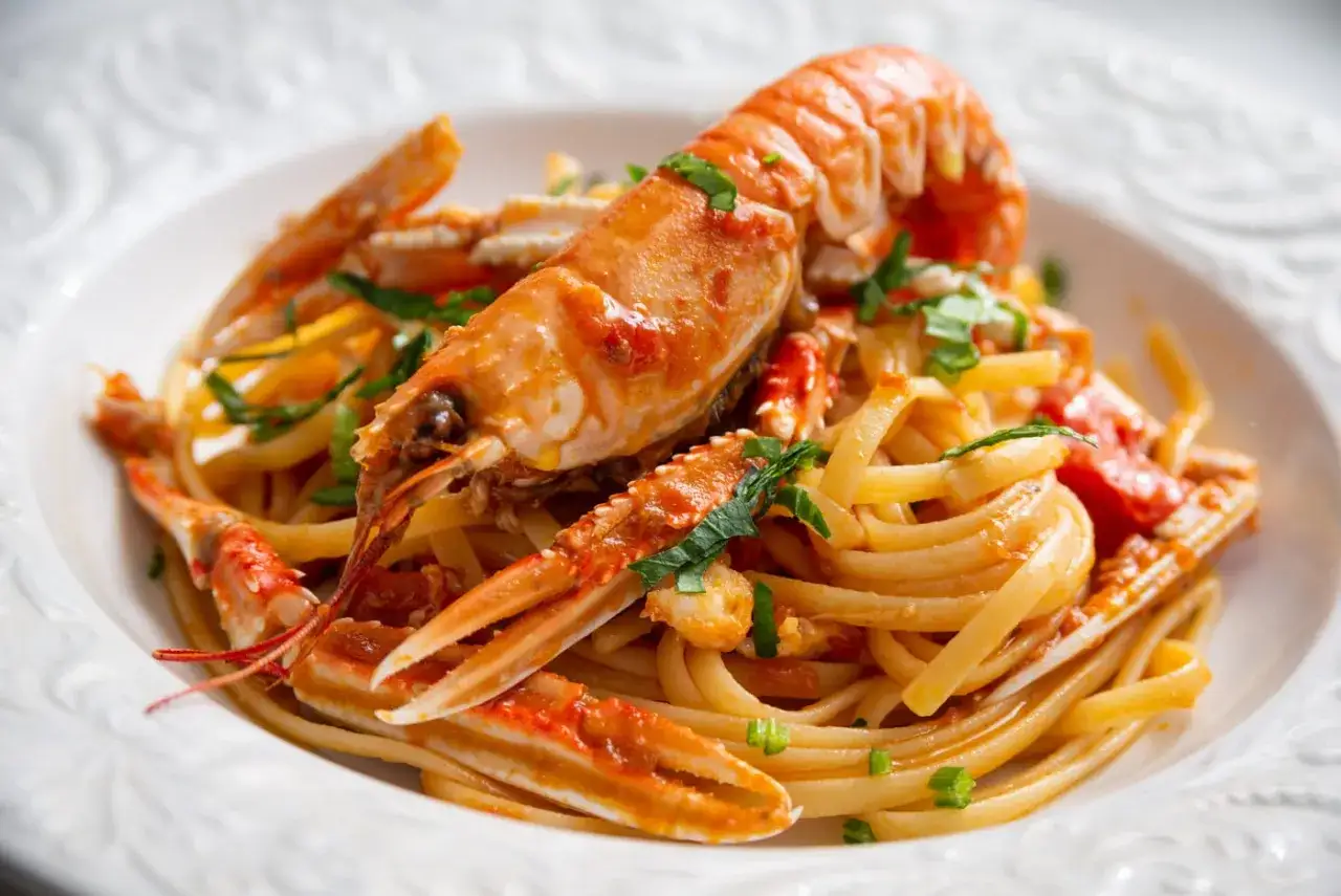 Un piatto invitante di linguine agli scampi, con pasta fresca e scampi succulenti conditi con un sugo saporito e prezzemolo tritato.