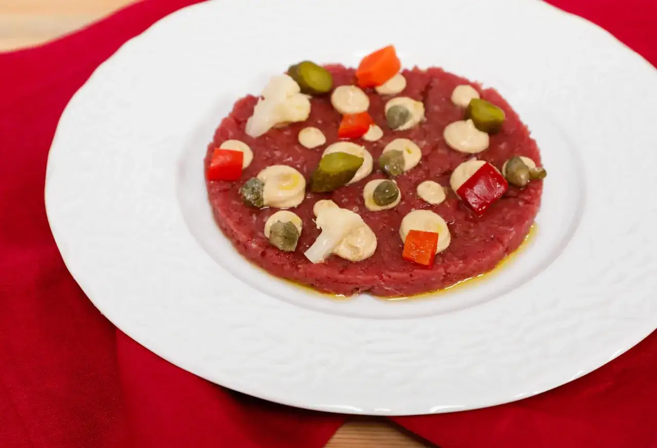 Deliziosa battuta di fassona cruda, guarnita con capperi, cetriolini, peperoni rossi e una salsa chiara.