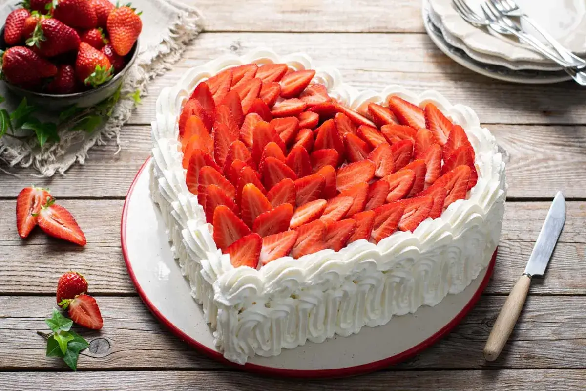 Una torta festa della mamma a forma di cuore, ricoperta di panna montata e fragole fresche affettate. Perfetta per celebrare l'amore.