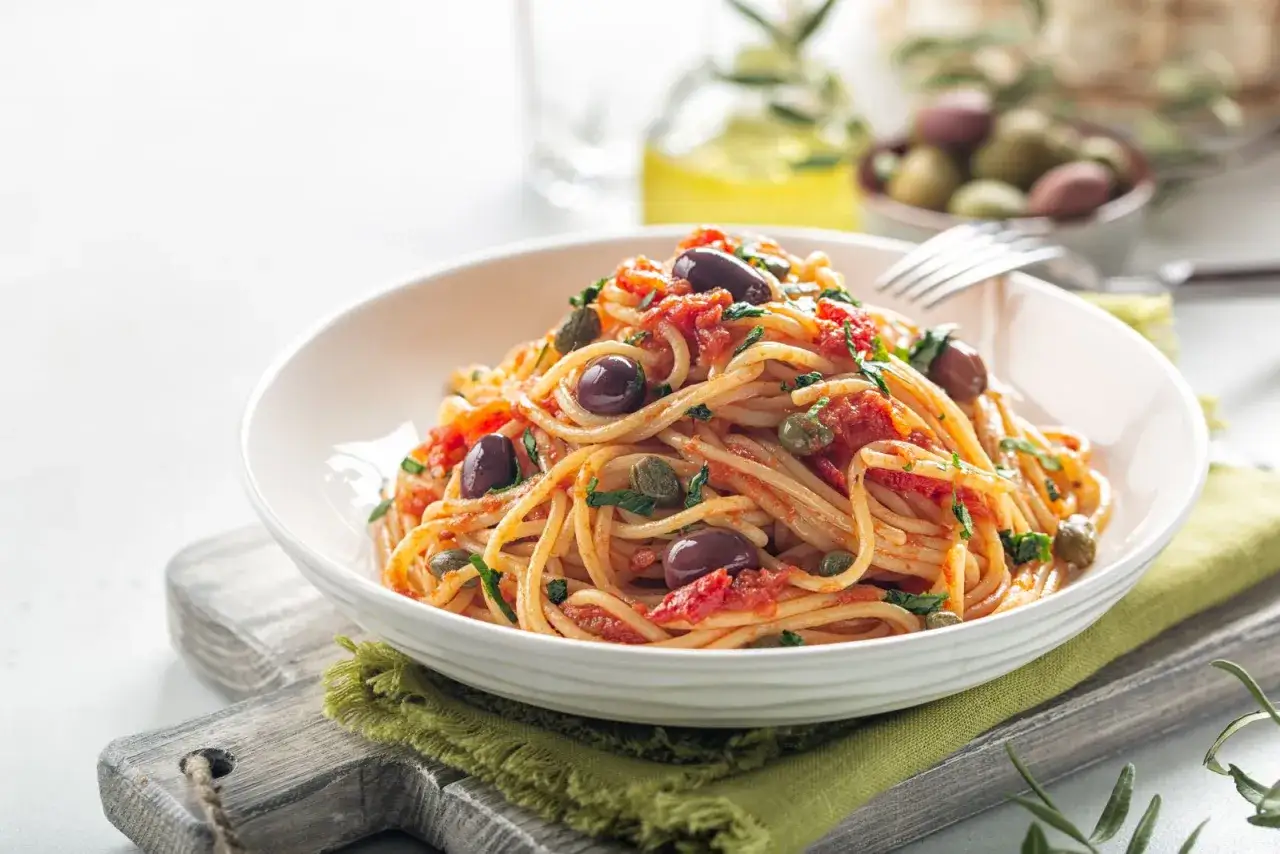 Spaghetti alla ghigliottina con pomodoro, olive nere e capperi, un piatto che fa venire l'acquolina in bocca.