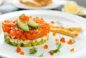 Tartare di salmone e avocado, un'idea per antipasti velocissimi senza cottura, guarnita con uova di pesce e cetriolo.