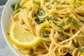 Un piatto invitante di spaghetti al limone, guarnito con scorza di limone e basilico fresco.
