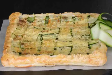 Torta salata con pasta sfoglia e zucchine a griglia, ricoperta di formaggio fuso e guarnita con fettine di zucchina fresca.