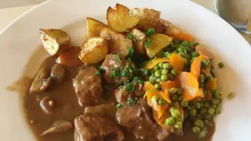 Un saporito spezzatino con piselli, carote e patate arrosto, guarnito con prezzemolo fresco.