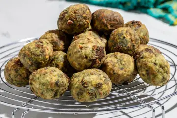 Pile di polpette ricotta e spinaci dorate e appetitose su una griglia metallica.