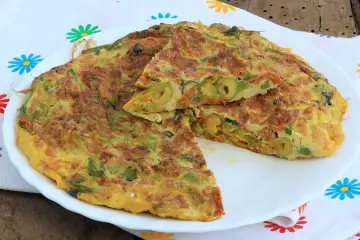 Frittata con fiori di zucca, carote e olive, tagliata a spicchi su un piatto bianco, con un tovagliolo fiorato sullo sfondo.
