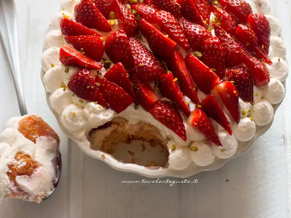 Delizioso tiramisù alle fragole, con panna montata, fragole fresche e pistacchi. Una fetta è già servita su un cucchiaio.
