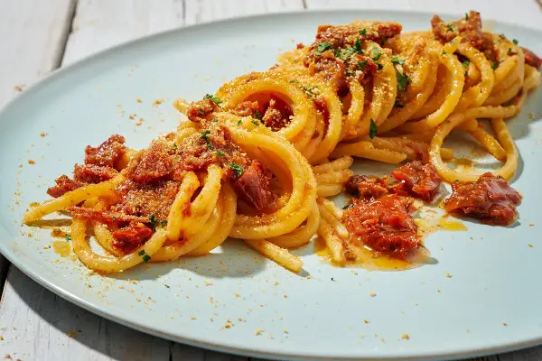 Spaghetti alla ghigliottina conditi con pomodorini secchi e pangrattato, un piatto invitante e saporito.