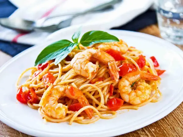 Un piatto invitante di spaghetti con gamberetti succulenti e pomodorini freschi, guarnito con basilico.