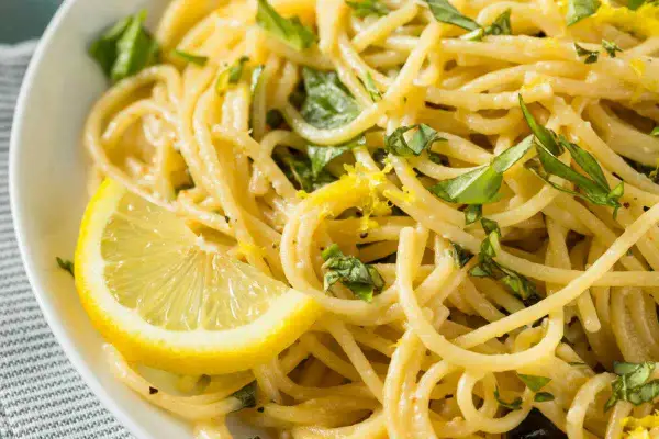 Un piatto invitante di spaghetti al limone, guarnito con scorza di limone e basilico fresco.