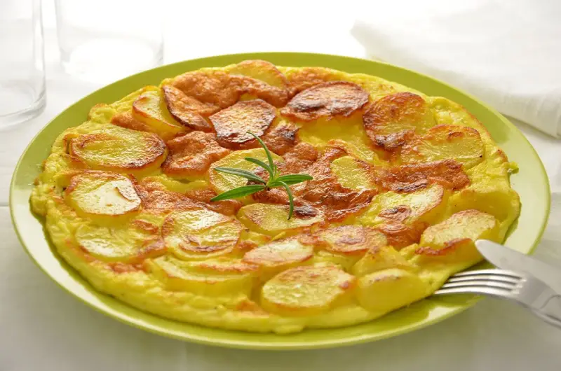 Frittata di patate dorata e gustosa, guarnita con rosmarino fresco, servita su un piatto verde.