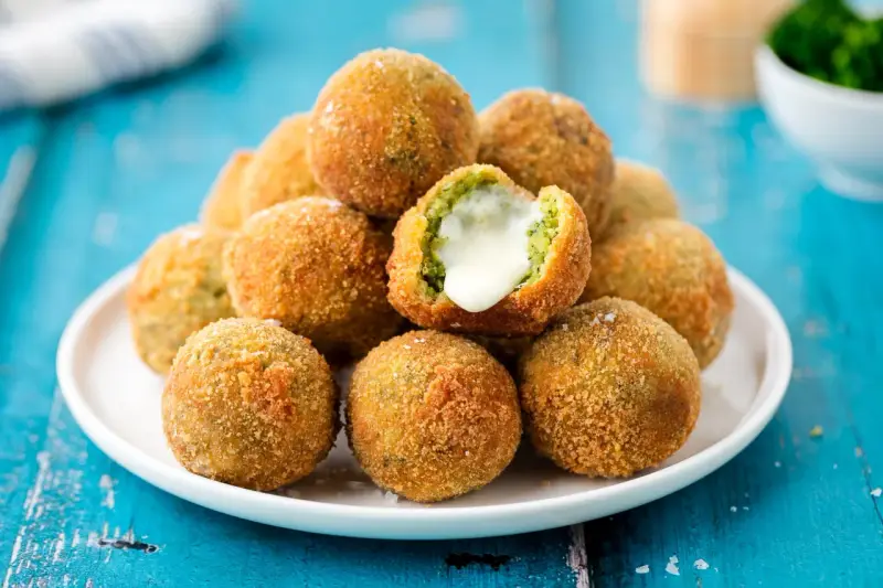 Pile di polpette di broccoli dorate e croccanti, una con il cuore filante di formaggio.