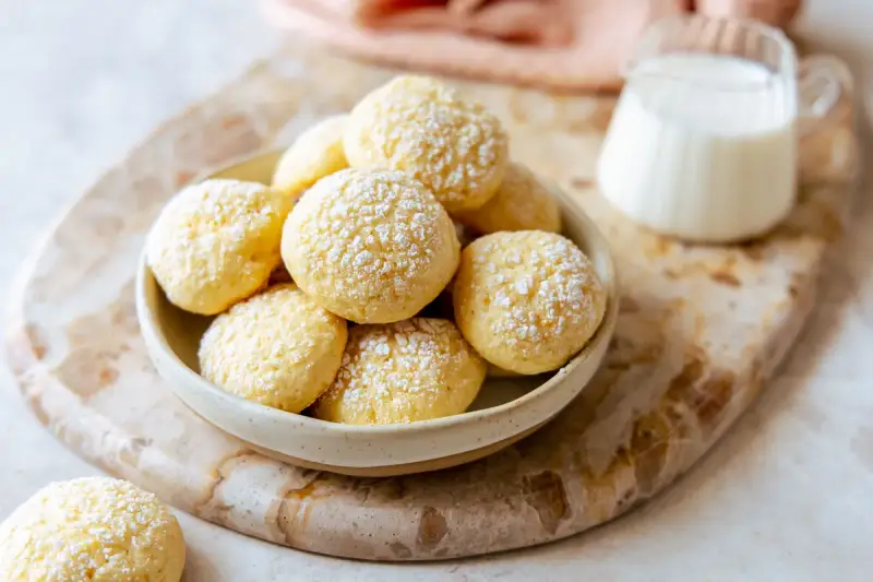Biscotti da inzuppo spolverati di zucchero a velo in una ciotola, pronti per essere gustati con un bicchierino di latte.