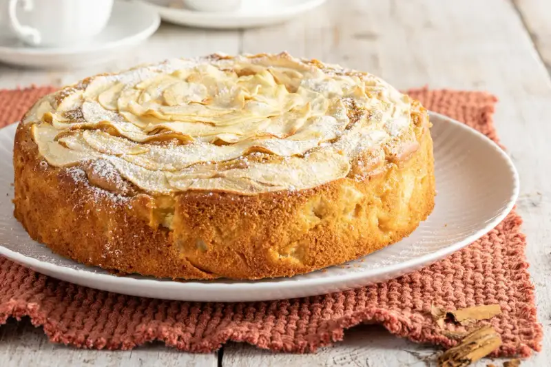 Deliziosa torta di mele senza burro, con mele a rosa sulla superficie e una spolverata di zucchero a velo. Perfetta per una colazione leggera.