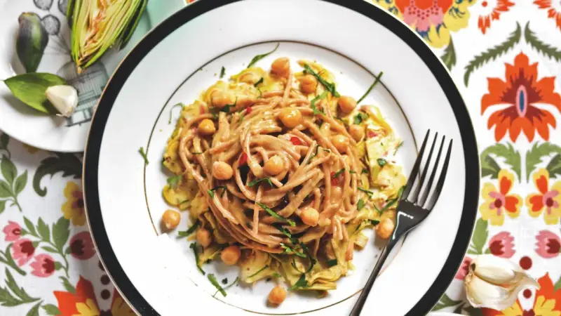 Un piatto invitante di pasta con carciofi alla siciliana, arricchito da ceci e erbe fresche, su un tovagliolo fiorito.