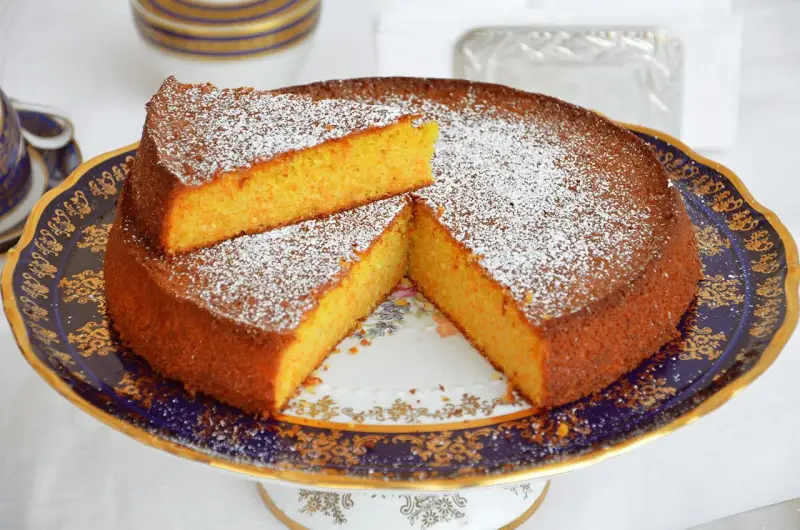 Deliziosa torta carote e mandorle, spolverata di zucchero a velo, servita su un elegante alzata.