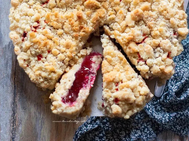Torta con marmellata, con crosta friabile e ripieno rosso brillante. Una fetta mostra la consistenza succosa.