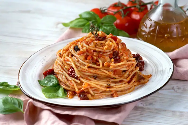 Un piatto di spaghetti conditi con un sugo rosso ricco di pomodori secchi, aglio e basilico fresco.